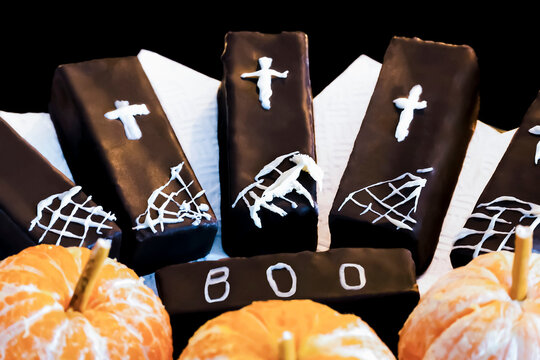 Large chocolates decorated with children's drawings of white icing sugar in the theme of Halloween. Crosses and cobwebs on cakes covered with brown chocolate. Decorating food Halloween.