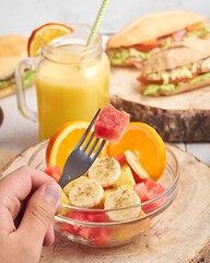 Ensalada de frutas con sandia en cubierto y naranja, sandia, plátano y piña con mano colocando polvo de grillo proteico