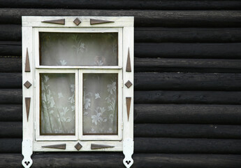 The window of a log country house is decorated with a simple pattern