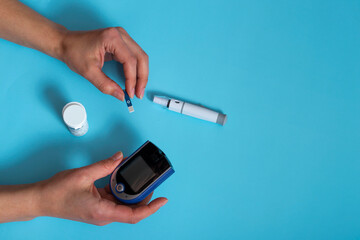 woman measures blood sugar with a glucometer.Diabetes concept on blue background