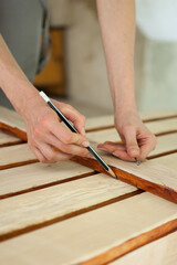 Female hands are making some marks on wooden plank for future holes using pencil for assembling bench, gender equality, feminism, do it yourself concepts.