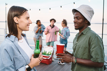 Young contemporary couple with drinks looking at one another with smiles against their friends