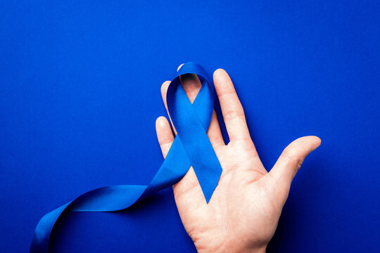 Blue ribbon. Awareness prostate cancer of men health in November. Blue ribbon in hands isolated on deep blue background. Symbol of oncology affected man. Copy space.