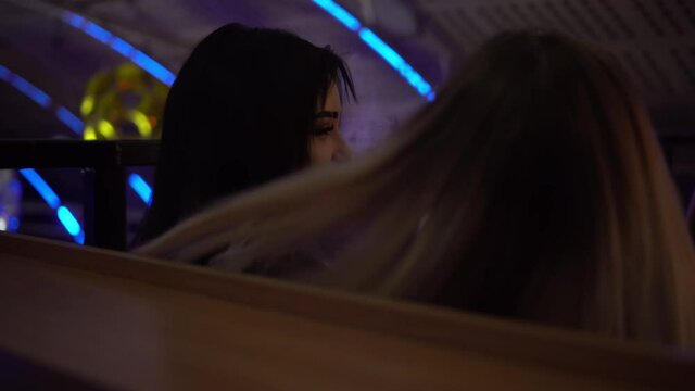 a sexy model of a Caucasian girl in neon, releasing the smoke of an electronic cigarette or vape. Focused close-up of a young woman's face in ultraviolet blue light. Night club, party. Rear view.