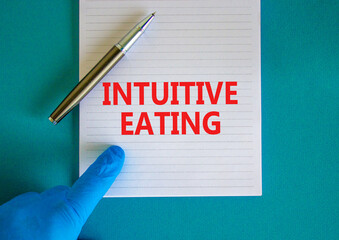 Intuitive eating symbol. White note with words Intuitive eating, beautiful blue background, doctor hand and metallic pen. Medical and intuitive eating concept.