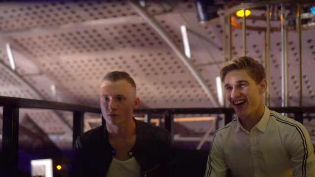 Guys and girls relax at a table in a nightclub. They laugh, drink, talk . Celebration of the holiday. A party. The concept is not a healthy lifestyle. Alcoholism.