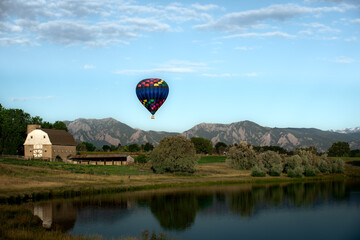 A hot air balloon rise above a barn and the Flatirons near Boulder, Colorado  - obrazy, fototapety, plakaty