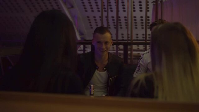 Guys and girls relax at a table in a nightclub. They laugh, drink, talk . Celebration of the holiday. A party. The concept is not a healthy lifestyle. Alcoholism.
