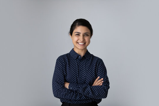 Head Shot Portrait Smiling Young Indian Woman With Arms Crossed Standing On Grey Studio Background Isolated, Confident Successful Businesswoman Or Student With Folded Hands Looking At Camera