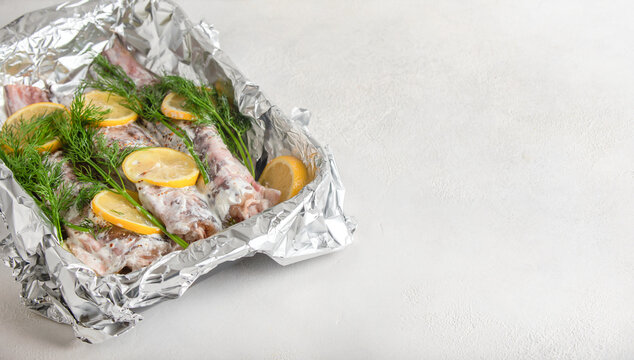 Congrio fish in sour cream filling is laid out on foil, sprinkled with seasoning, lemons and dill on top. High quality photo
