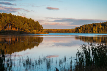 Fototapeta premium The landscape of the autumn coniferous forest and the sky in the colors of the sunset with a reflection in the water of the lake.