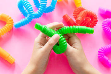 colorful antistress sensory toy fidget push pop tube in kid's hands on pink background