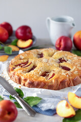 Torta di pesche decorata con nocipesche  e mandorle a lamelle su un tavolo con nocipesche intere o tagliate a fette  e foglie
