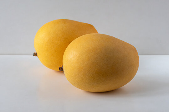 Two ripe sweet mangoes with yellow skin, on a light background