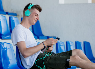 Young teen boy with headphones sitting in blue sit on stadium tribune