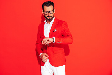 Portrait of handsome confident stylish hipster lambersexual model. Sexy modern man dressed in elegant suit. Fashion male posing in studio near red wall in spectacles