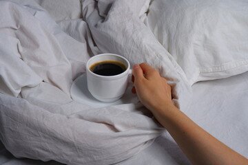 Girl holding a cup of coffee in bed. Breakfast in bed. Interior. Cosiness.