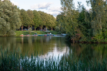 Fototapeta na wymiar Lake in the park. Green trees, islands, on a pond. People are relaxing and boating. Reflection on the water. Day. Autumn. Russia.