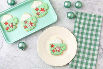 Homemade Christmas Cookies Shaped Like Coffee Mugs on White Background with Christmas Ornaments, Green Checked Towel, Green Cookie Sheet, One on White Plate
