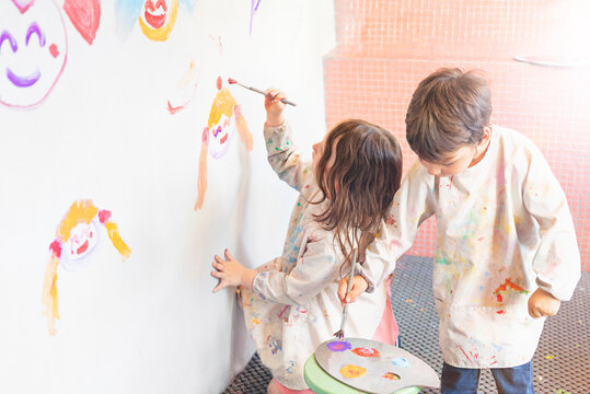 Little kids draws with paints on a white wall, back view