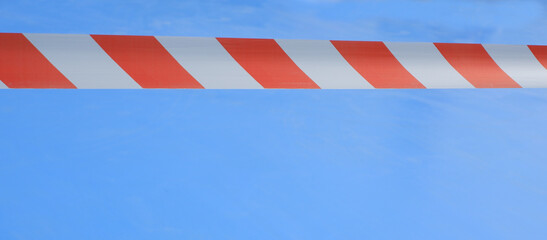 Signal red-white tape on a blue background. Red And White Warning Tape On A Blue.