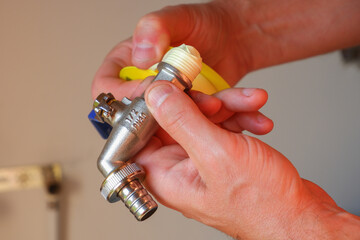 Replacement of the watering tap. The plumber holds a new faucet in his hand and winds the sealing tape around the threads.