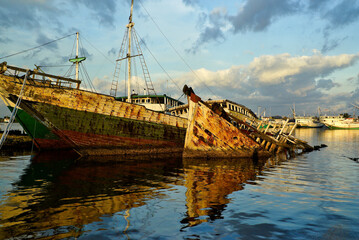 Traditional wooden sailing ships (Bugis pinisi) are reflected in the still waters of Paotere Harbor.