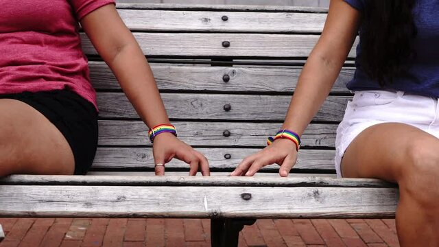 Two hands together with LGBT bracelets in the park