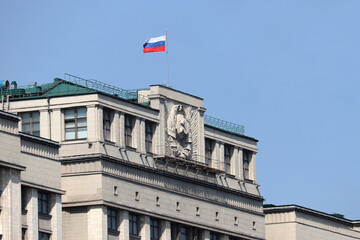 Russian flag on the parliament building in Moscow on background of blue sky. Facade of State Duma...