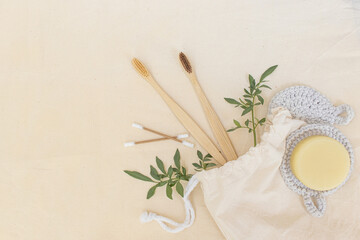 Biodegradable beauty and hygiene items coming out of a natural raw cotton bag: bamboo toothbrush, dye-free bar soap, cotton swabs, eco pads for skin care and natural green leaves