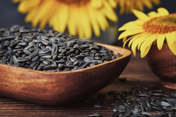 Wooden bowl of sunflower seeds and beautiful yellow sunflowers on background. - 457918897