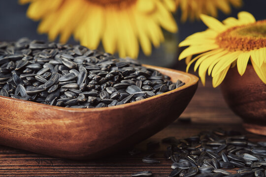 Wooden bowl of sunflower seeds and beautiful yellow sunflowers on background.
