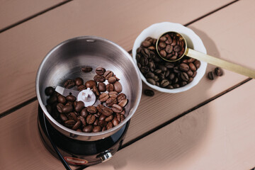 Coffee beans in a white plate on a wooden background and an electric coffee grinder. Iron spoon for coffee beans. Coffee content, coffee shop.