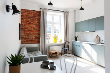 Small room with window in loft apartment in modern style with kitchen, living room and dining room. Stylish furniture in scandinavian design with table, chairs, sofa and bricky wall.