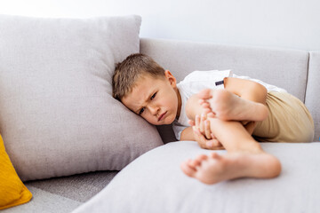 Cute angry boy. Morning home. Naughty little boy. Angry little boy frowned while sitting in bed and looking at camera. Angry boy with furrowed brows. Offended boy sitting on sofa