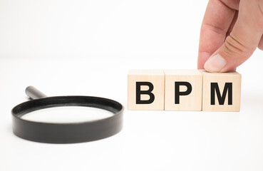 bpm text wooden cube blocks and hand holding magnifying glass on table background.