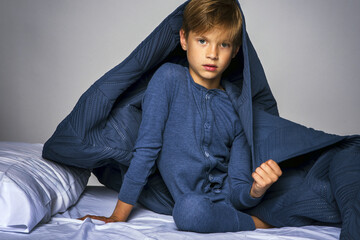 Young boy in pajamas sitting up in bed with blanket over his head © 3Days2Go Media
