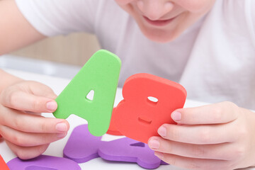 A kid learning letters and alphabet, he is sitting at a table and holding colorful foam letters in hands