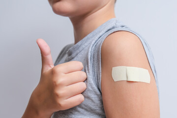 An arm of a boy with adhesive bandage plaster on it after vaccination showing thumb up, injection...