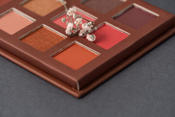 Artistic photography of cosmetics. Eye shadows and withe flowers on a grey background