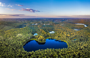 Aerial view of sunrise over a pine forest with lake. Foggy and colorful morning in countryside. © Viesturs
