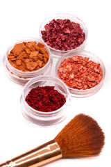 Creative photo of cosmetic swatches. Broken eye shadows in bronze and pink colours and make up brushes on a white background 