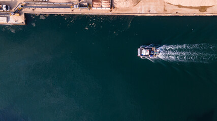 Aerial view of fishing boat moving through canal by industrial estate.