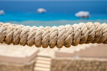 Close-up of horizontal marine rope in the center of the picture with bokeh background. Sunny day. Blurred background of blue water of the Red Sea with boats and stairs to the sea.