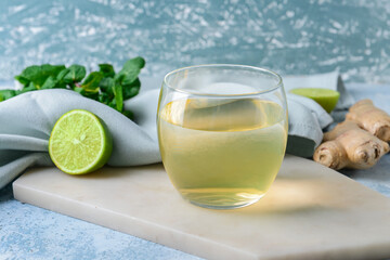 Glass of tasty juice with lime and ginger on color background