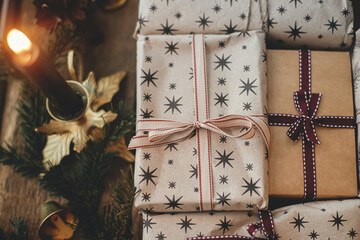 Merry Christmas ! Stylish christmas gifts wrapped in craft paper, vintage candles, fir branches and bells on rustic wood top view. Stylish scandinavian xmas presents, atmospheric winter time.