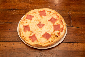 Italian mozzarella cheese pizza with pieces of cooked ham on wooden table