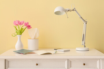 Stylish workplace with beautiful flowers and modern lamp near light wall