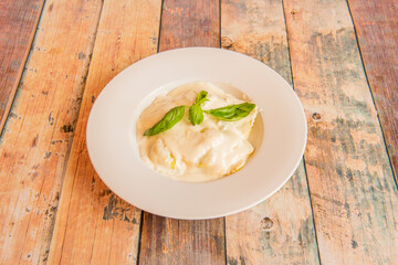 Ravioli stuffed with cheese covered with béchamel sauce and basil leaves on wooden table