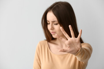 Stressed young woman showing STOP gesture on grey background. Concept of harassment
